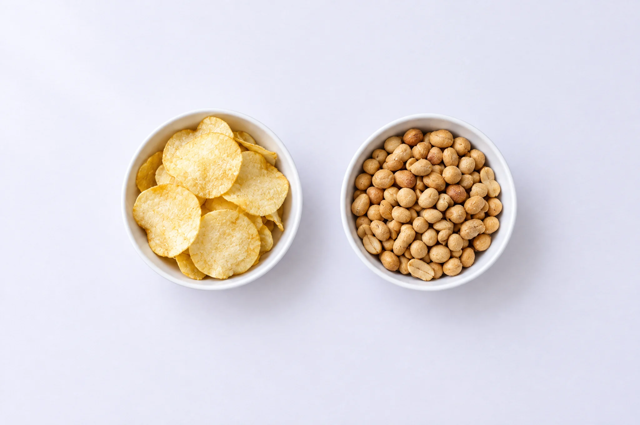 Two identical white bowls, one with crisps and one with peanuts